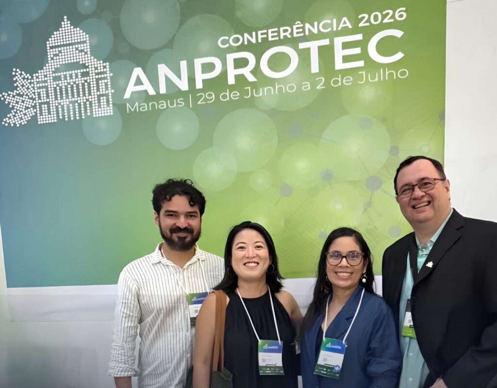 4 pessoas reunidas sorridentes. Prof. Filipe Saraiva, Superintendente; Profa. Katia Omura, Coordenadora de Propriedade Intelectual e Transferência Tecnológica; e Ailana Guta, Coordenadora do Parque Tecnológico Tecnolago, no campus de Tucuruí, da SInD UFPA. Logo atrás um painel em verde e azul com a nome "Anprotec 2026"